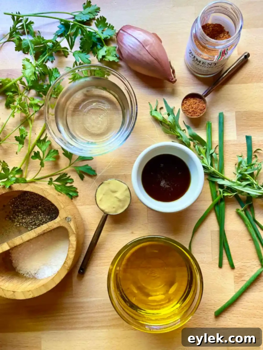 A glass jar filled with freshly made Classic French Dijon Vinaigrette, surrounded by ingredients like shallots, herbs, and a bottle of olive oil.